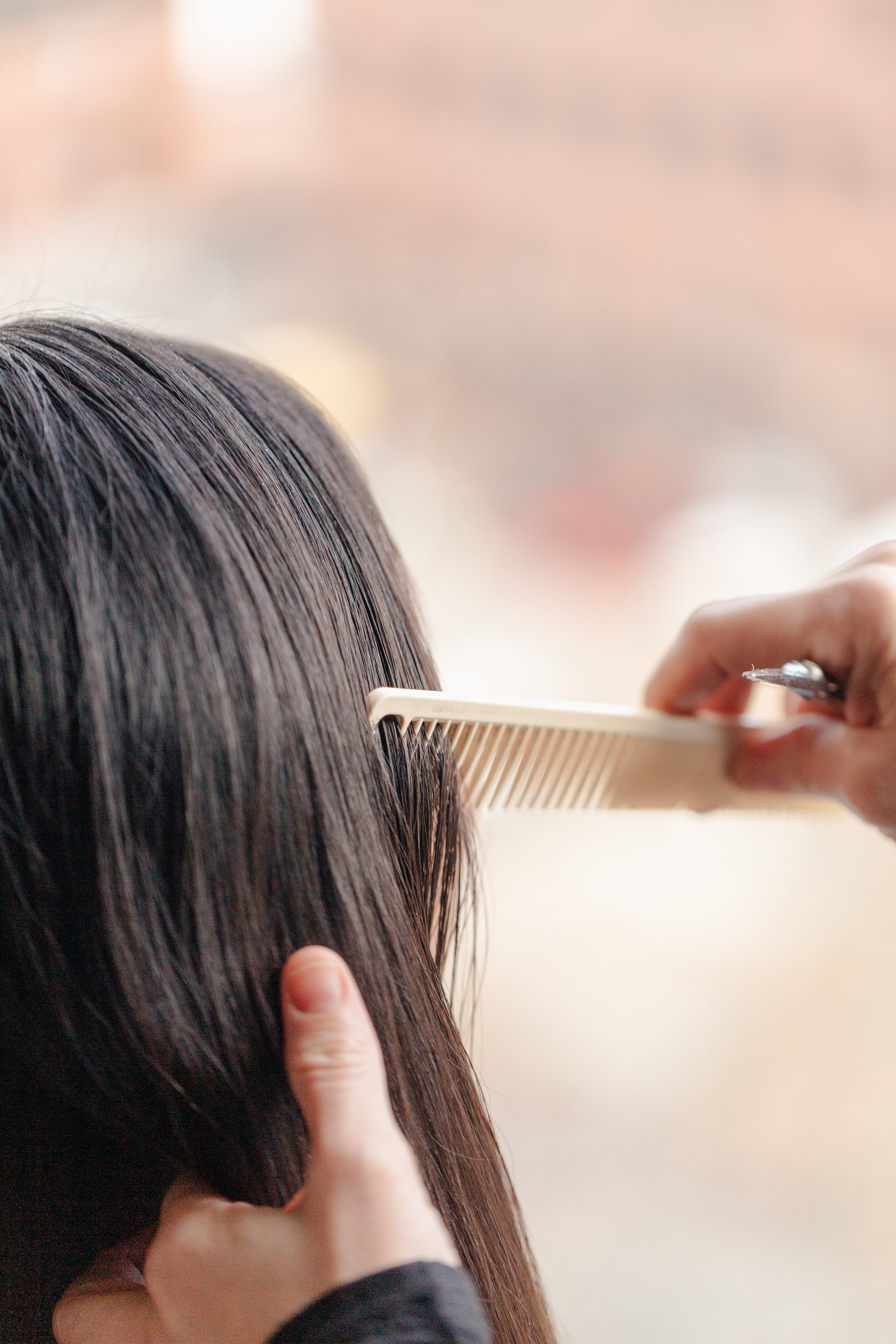 Hair stylist combing long, brown hair.